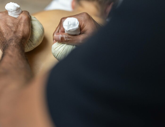 Eine Person erhält eine Jambira Pinda Sweda Behandlung mit warmen Kräuterstempeln im Kristall Spa.