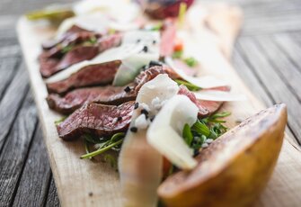 Auf einem Holzbrett liegen dünn geschnittenes Rindfleisch, Salat und Käse ansprechend angerichtet.