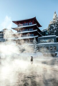 Der Chinaturm ragt über dem verschneiten See-Bad, aus dem Dampf aufsteigt, während eine Person durch das Wasser geht.