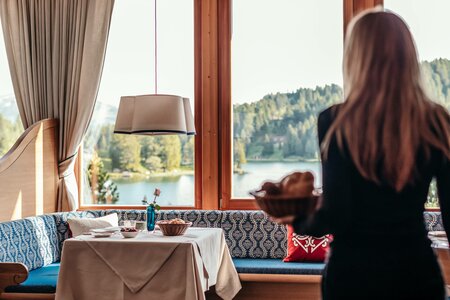 Eine Frau steht im Hotelrestaurant vor einer Fensterfront mit Blick auf den See und die bewaldeten Hänge.
