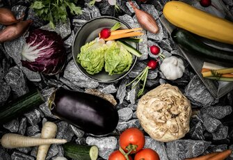 Verschiedene frische Gemüsesorten liegen auf dunklen Steinen arrangiert und zeigen Kulinarik mit regionalen Zutaten.