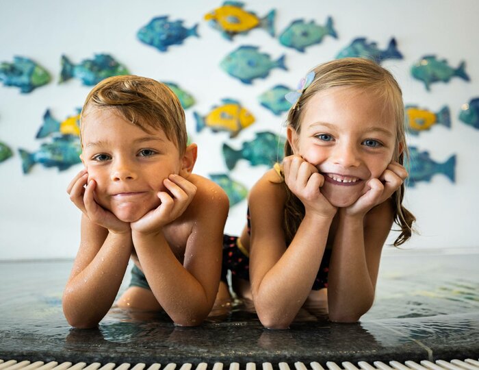 Children in a swim lesson at Hotel Hochschober Two children lie smiling at the pool edge during a swim lesson at Hotel Hochschober.