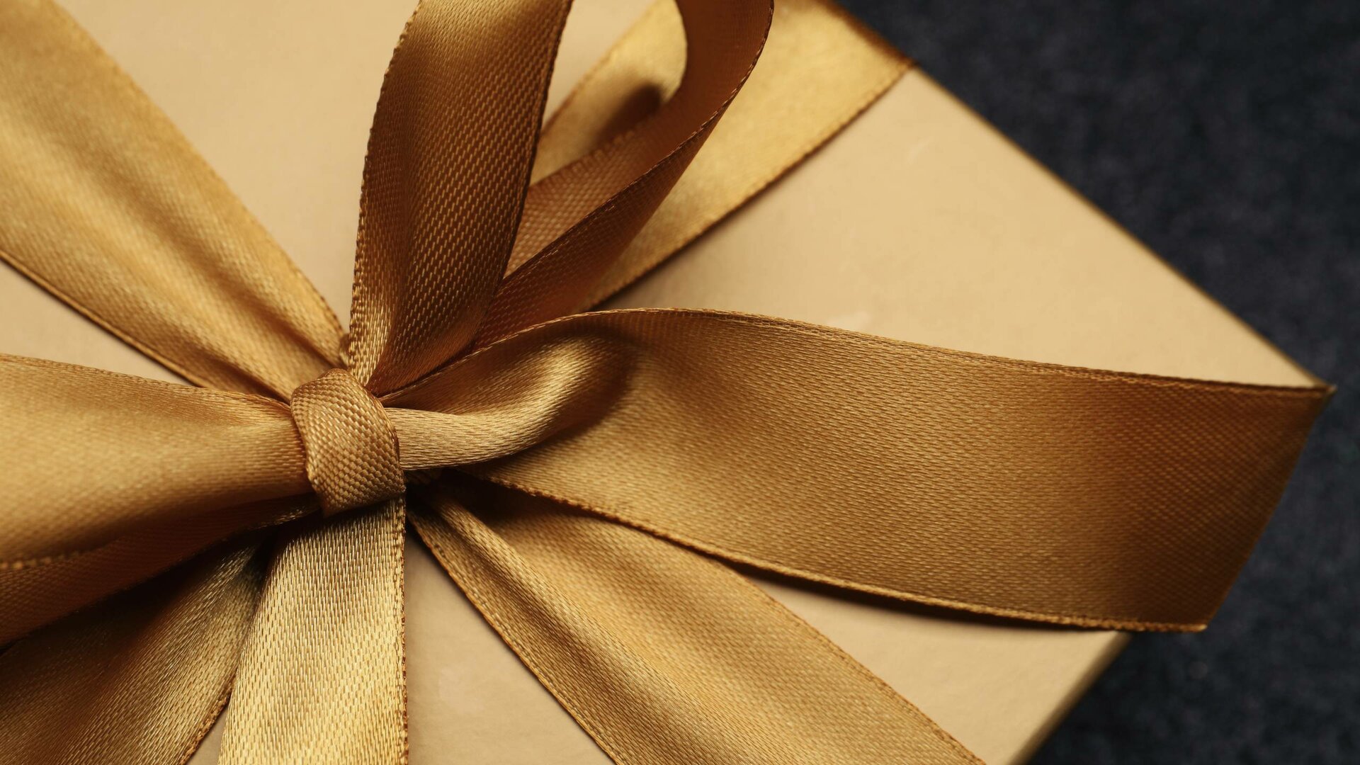Ein Geschenkumschlag mit goldener Schleife liegt auf dunklem Hintergrund.