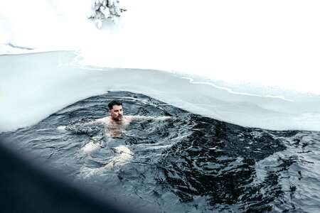 Ein Mann schwimmt in einem dunklen, eisigen See-Bad unter Schnee am Ufer.