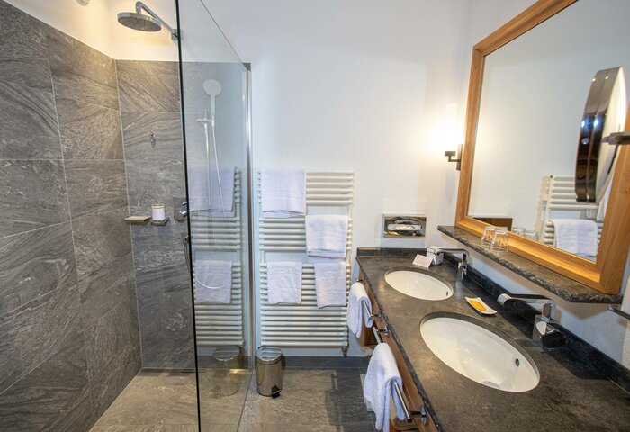 Comfort bathroom in Hotel Hochschober Modern bathroom with double sinks, a glass shower and dark tiles in the Comfort Bay Panorama Room.