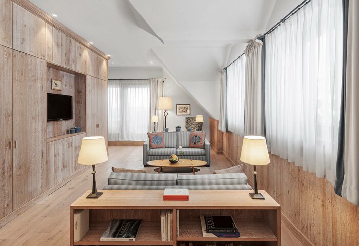 The Bergkristall Suite shows a bright living area with a sofa, reading lamps, wood walls and large windows.