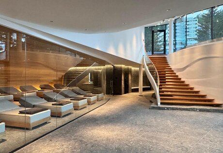 Ein moderner Wellnessbereich mit Liegen, Glaswand und Holztreppe im Hotel Hochschober.