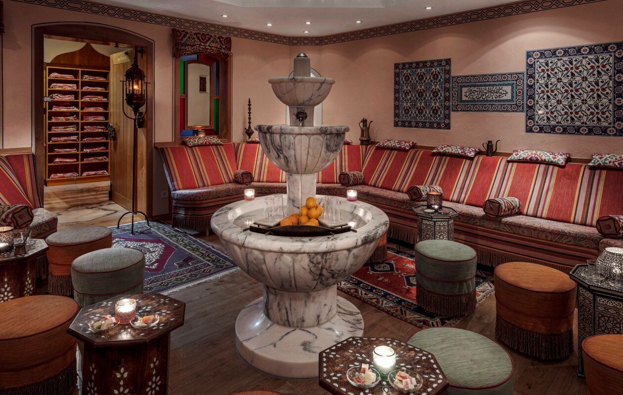 An oriental-style hamam with a marble fountain, seating benches and warm colours at Hotel Hochschober.