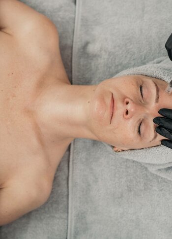 Eine liegende Person erhält im Kristall Spa eine Microneedling-Behandlung im Gesicht, während eine Fachkraft mit Handschuhen arbeitet.