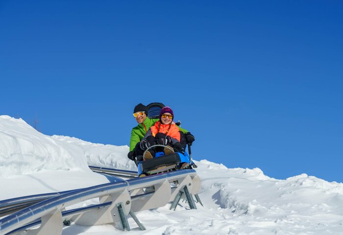 Der Nocky Flitzer fährt durch die verschneite Landschaft auf der Turracher Höhe, zwei Fahrgäste sitzen im Wagen.