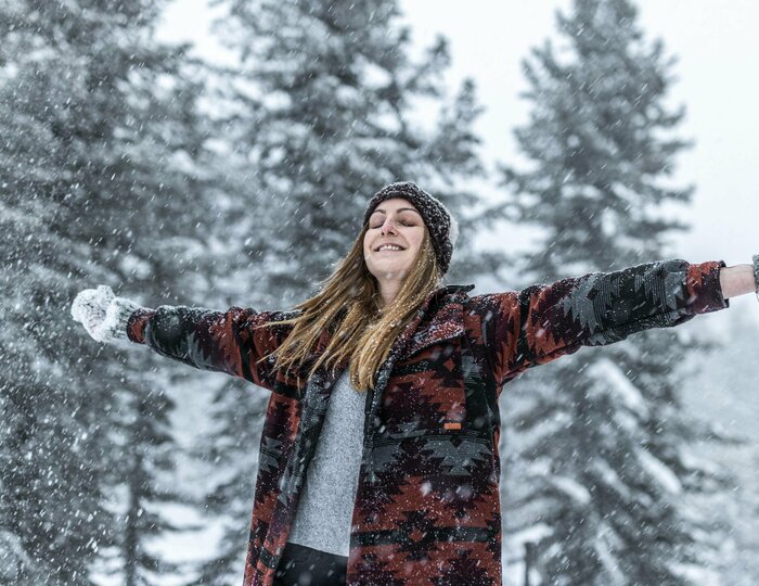 Winterfreude beim Schneespaziergang auf der Turracher Höhe Eine Frau steht mit ausgebreiteten Armen im Schnee vor verschneiten Tannen.