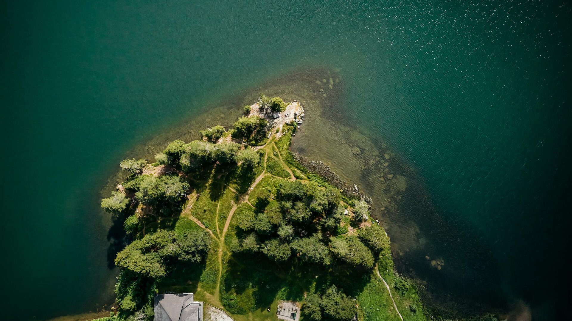 Aerial view of a wooded peninsula in a turquoise lake with paths and shoreline.