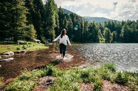Eine Frau geht am Ufer des Turracher Sees durch das flache Wasser, umgeben von Wald und Bergen.
