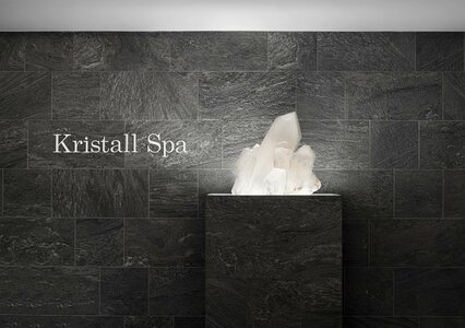 Ein beleuchtetes Kristallobjekt steht auf einem dunklen Sockel vor einer Steinwand mit der Aufschrift Kristall Spa.