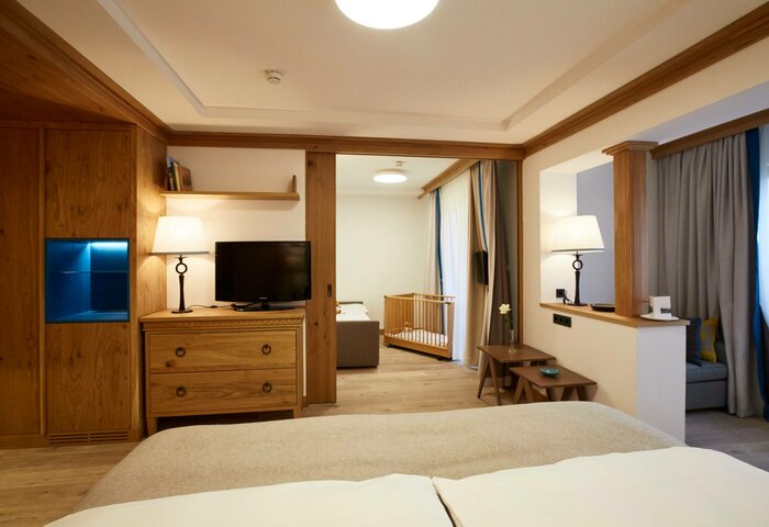 A family apartment studio with wooden furniture, a TV, seating area and a view into the adjoining sleeping area.