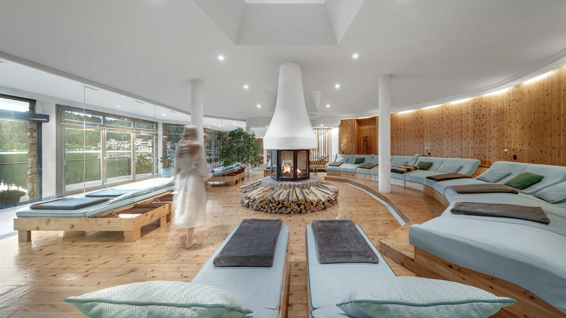 Ein heller Ruheraum mit Liegen, zentralem Kamin und großen Fenstern im Kristall Spa des Hotel Hochschober.