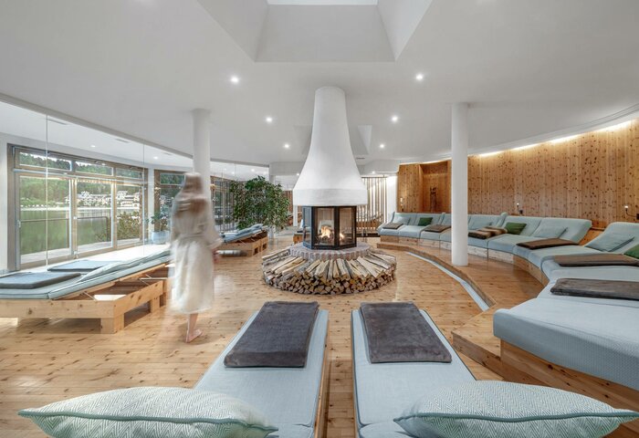 Ein heller Ruheraum mit Liegen, zentralem Kamin und großen Fenstern im Kristall Spa des Hotel Hochschober.