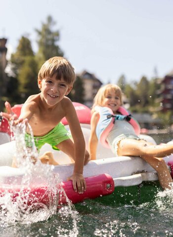 A woman and two children sit on a pedal boat on the lake while water splashes around it.