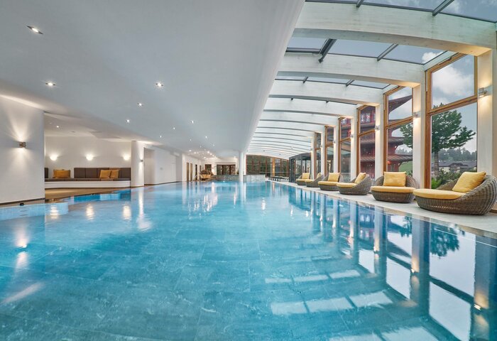 A bright indoor pool with calm water, loungers by the windows, and an outside view.