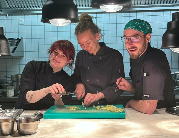 Drei Personen bereiten gemeinsam in einer Hotelküche Zutaten an der Arbeitsfläche zu.