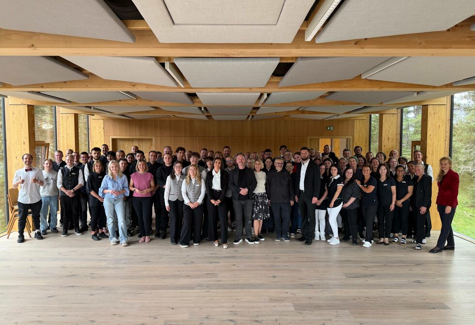 Eine große Gruppe von Mitarbeitenden steht in einem hellen Raum des Hotel Hochschober für ein gemeinsames Teamfoto.