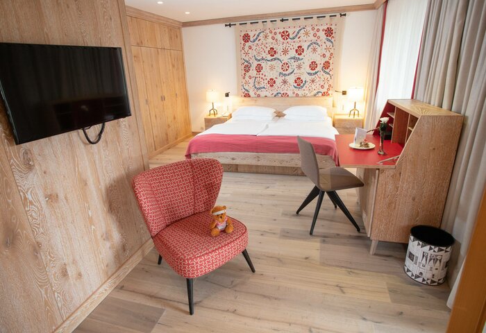 Ein Superior-Doppelzimmer im Stammhaus mit Bett, Schreibtisch, TV, Sessel und heller Holzausstattung.