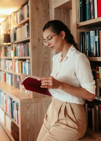 A woman reads in a wood-paneled hotel library while leaning against the bookshelves.