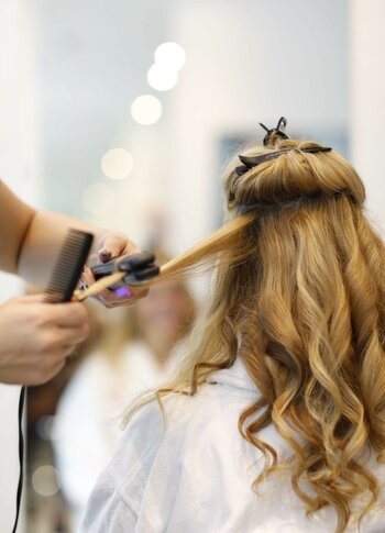 Eine Friseurin föhnt einer Kundin im weißen Mantel langes blondes Haar im Kristall Spa.