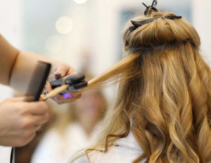 Hair spa blow-dry styling at Kristall Spa A stylist blow-dries a woman's long blonde hair while she sits in a white robe at the spa.