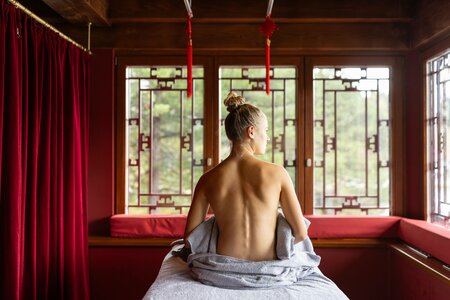 Eine Frau sitzt mit freiem Rücken auf einer Liege im Chinaturm mit roten Vorhängen und Holzwänden.
