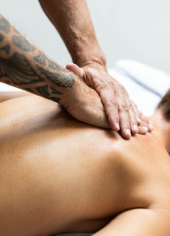 Eine Frau liegt mit dem Gesicht nach unten auf der Massageliege, während der Therapeut ihren Rücken mit den Händen behandelt.