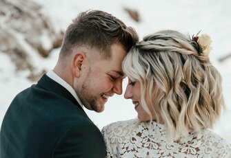 A bride and groom lean closely together and smile in a winter setting.
