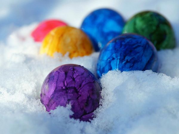 Mehrere bunt gefärbte Ostereier liegen im Schnee