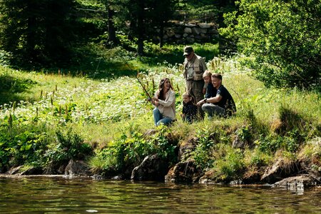 Eine kleine Gruppe sitzt am Ufer des Turracher Sees inmitten einer grünen Wiese und dichtem Wald.