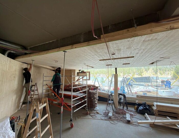 Im Innenraum der Baustelle laufen Ausbauarbeiten, mit Gerüst, Leitern, Kabeln und großen Fenstern zum Außenbereich.