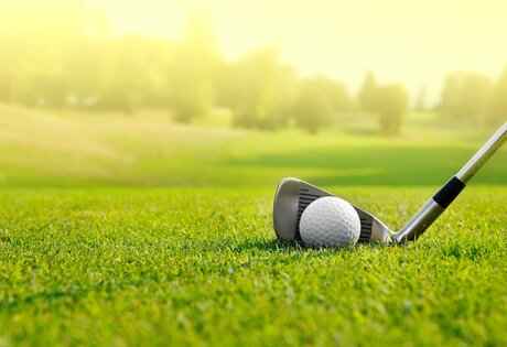 Ein Golfball liegt neben dem Eisen auf dem kurz geschnittenen Rasen des Golfplatzes.