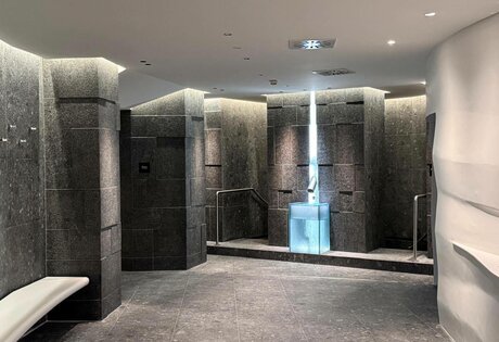Ein moderner Wellnessbereich mit dunklen Steinwänden, Leuchten und einer Sitzbank im Hotel Hochschober.