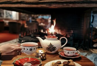 Ein gedeckter Teetisch mit Teekanne, Tassen und Gebäck vor dem Kamin.