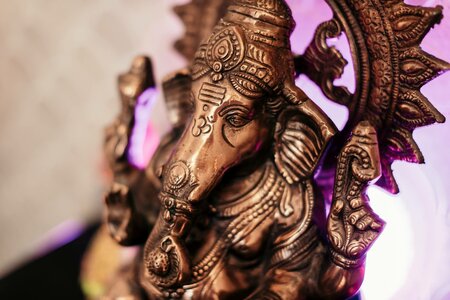 Eine bronzefarbene Ganesha-Statue ist im warmen Licht mit violettem Hintergrund aus der Nähe zu sehen.