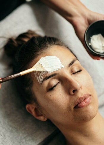Eine Frau erhält im Liegen eine Gesichtsbehandlung mit Pinsel und Schale im Kristall Spa.