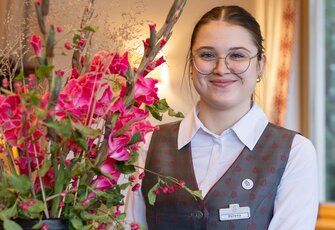Eine Mitarbeiterin steht neben einem farbenfrohen Blumenarrangement in der Hotellobby.