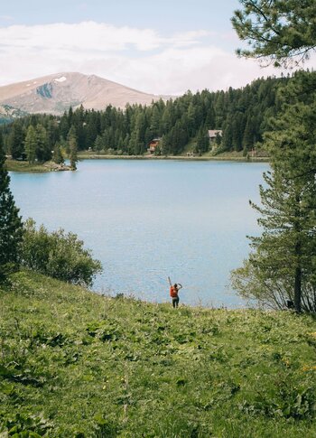 Sommerfrische am See auf der Turracher Höhe Eine Person steht am Ufer des Sees vor Wald und Bergkulisse und hält die Arme nach oben.