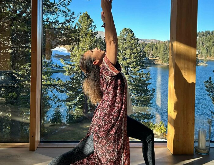 Yoga with lake view at Hotel Hochschober A woman practices yoga on a mat in front of large windows overlooking the lake and forest.