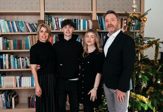 Eine Familie steht vor einem Bücherregal neben einem geschmückten Weihnachtsbaum in der Hotelbibliothek.