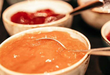 Mehrere Schalen mit Fruchtaufstrichen stehen auf einem Frühstücksbuffet, im Vordergrund ein heller orangefarbener Aufstrich.