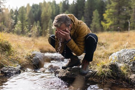 Ein Wanderer kniet am Bergbach und wäscht sich das Gesicht in der Natur.