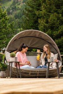 Zwei Frauen sitzen in einer überdachten Lounge im Freien und trinken auf der Terrasse des Hotel Hochschober.