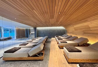 A modern relaxation room with several loungers, a wood ceiling and a glass front facing outside.