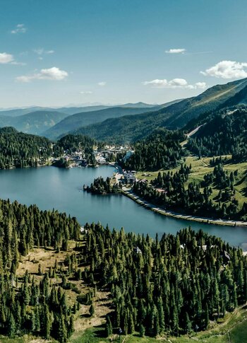 Blick über den Turracher See mit Wäldern, Almen und Bergen in den Nockbergen.