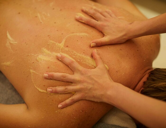Hände massieren den Rücken einer Person mit einer Paste während der Udvarthana-Behandlung im Spa.
